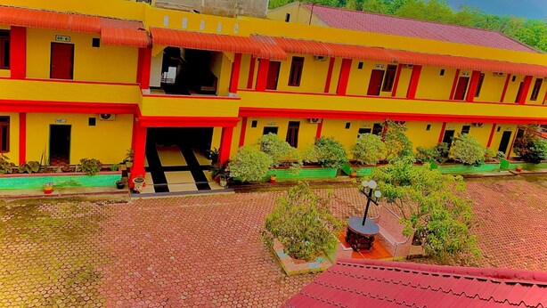 Un edificio de dos pisos con fachada roja y amarilla, varias ventanas y un patio empedrado con macetas.