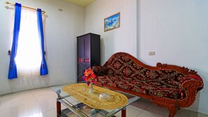 Una sala de estar con una mesa de centro de vidrio, un sofá rojo con estampado, una cortina azul y un cuadro en la pared.