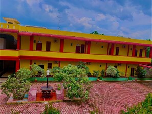 A two-story yellow building with red accents, a tiled courtyard, and green plants. - Hotel Rembulan (Tebing Tinggi)