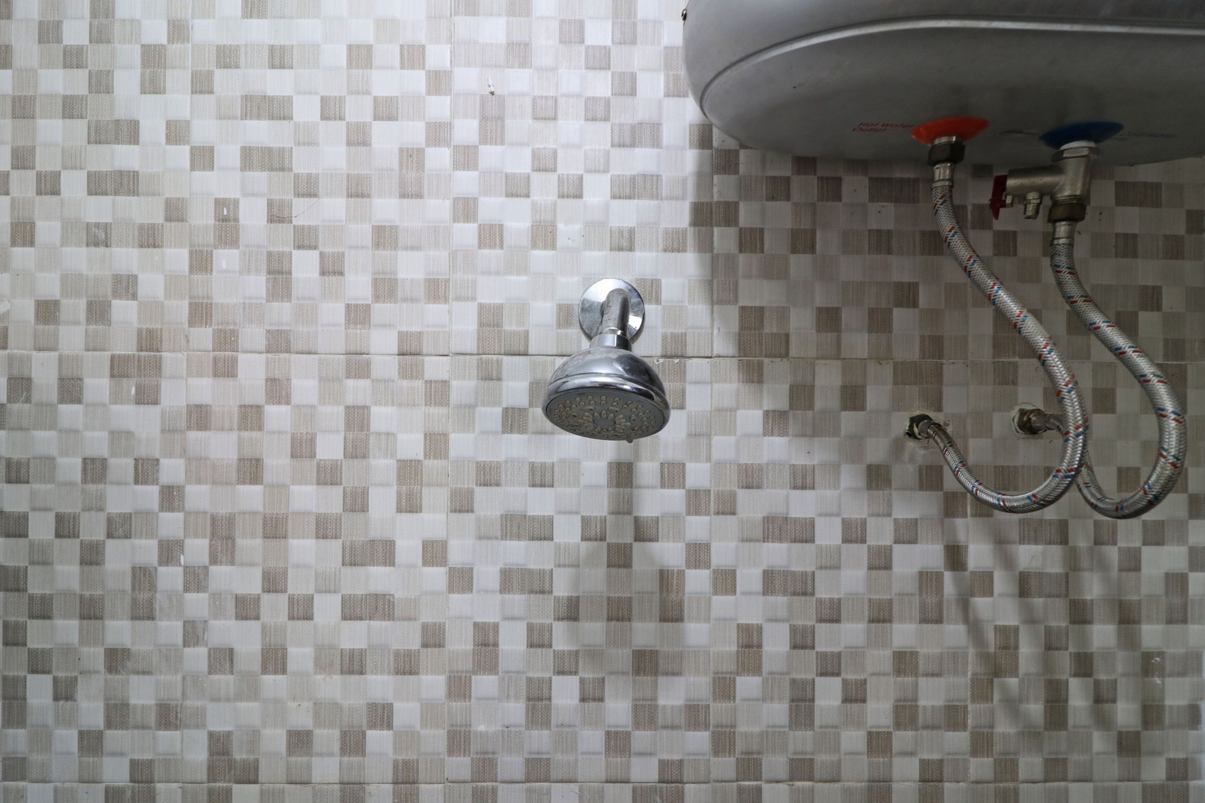 Douchekop bevestigd aan een betegelde muur, met een zichtbare waterleiding.