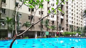 A swimming pool with blue tiles, surrounded by a multi-story building with balconies and greenery. - Inkubus Gateway Apartment Ahmad Yani by Ridwan (Bandung)