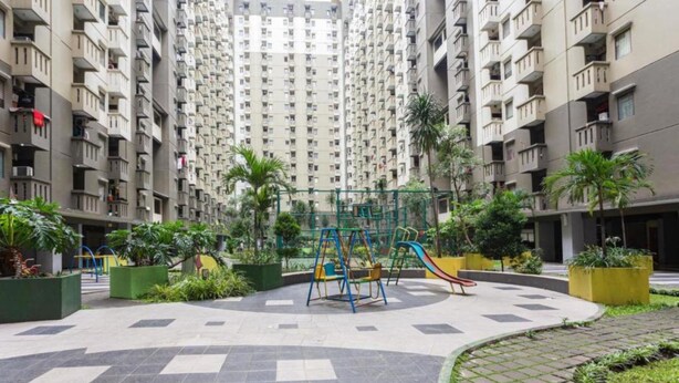 A residential building with multiple balconies, a playground with swings and slides, and surrounding greenery. - Inkubus Gateway Apartment Ahmad Yani by Ridwan (Bandung)