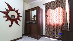 A room with a sun-shaped mirror, a wardrobe, patterned curtains, and a blue chair. - Inkubus Gateway Apartment Ahmad Yani by Ridwan (Bandung)