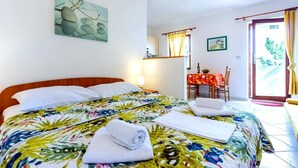 A hotel room with a bed, a table with a red tablecloth, a chair, and a door leading to the outside. - Studio apartment in Baška with Seaview, Balcony, Air condition, WIFI (3494-2) (Baška)