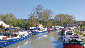 A narrow canal with boats docked along the sides, surrounded by trees and buildings.