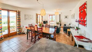 A dining area with a table and chairs, a sofa, a TV, and a large window with a view.