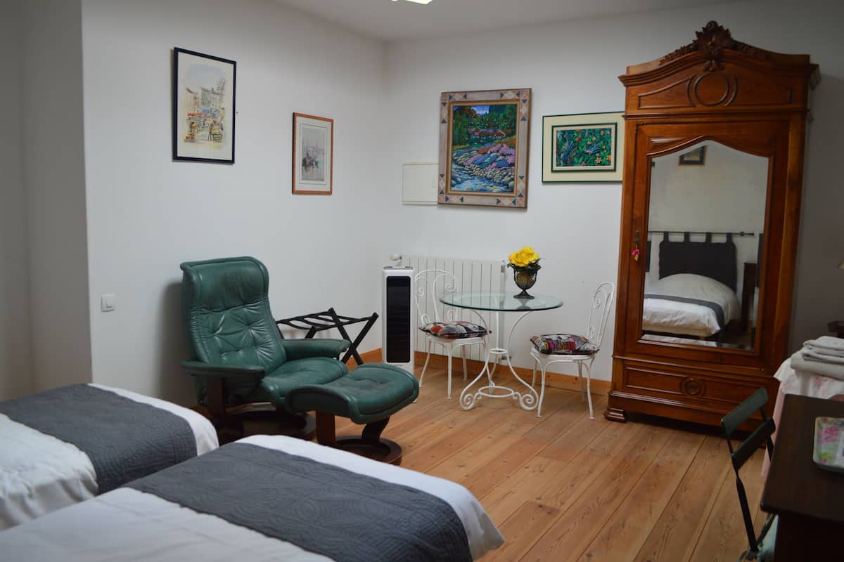 Una habitación con dos camas, una silla verde, una mesita con un florero y un espejo grande.
