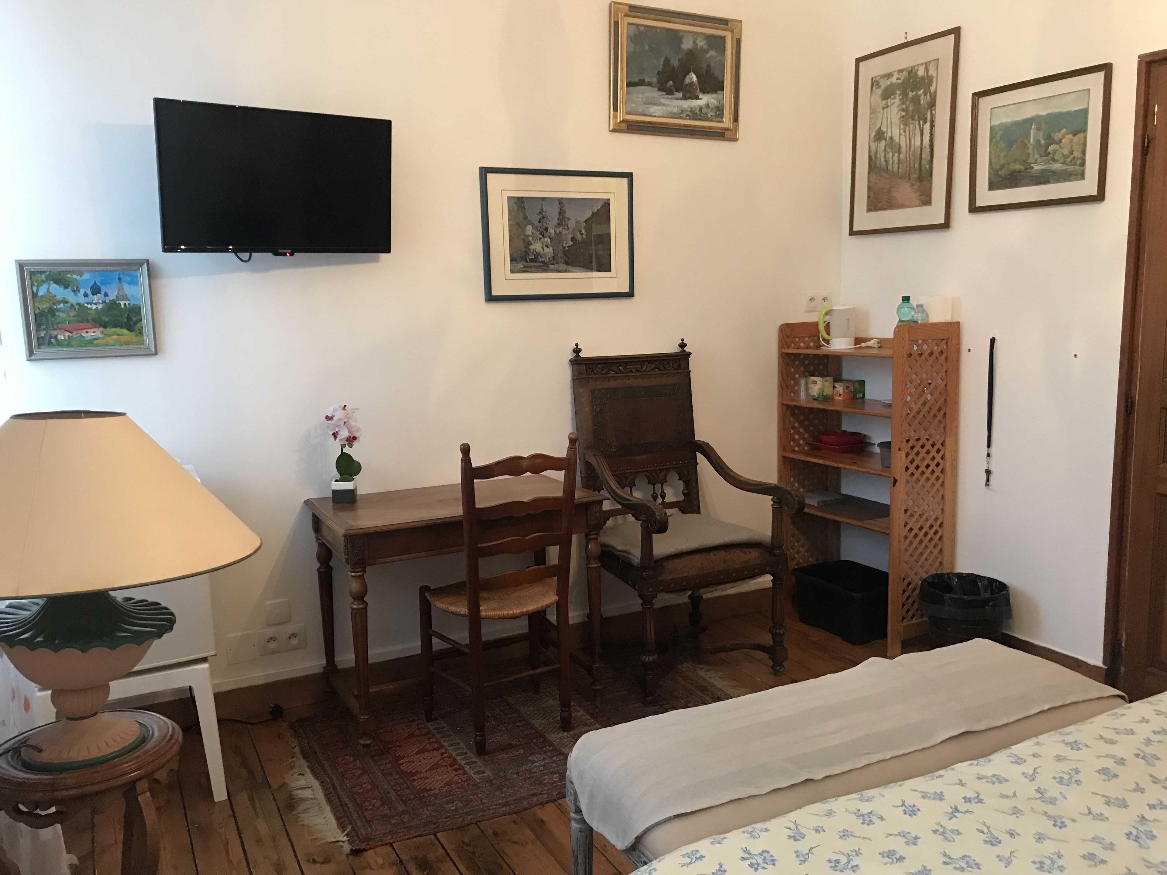 Une pièce comprenant un lit, un bureau avec une chaise, un téléviseur et des tableaux encadrés accrochés au mur.
