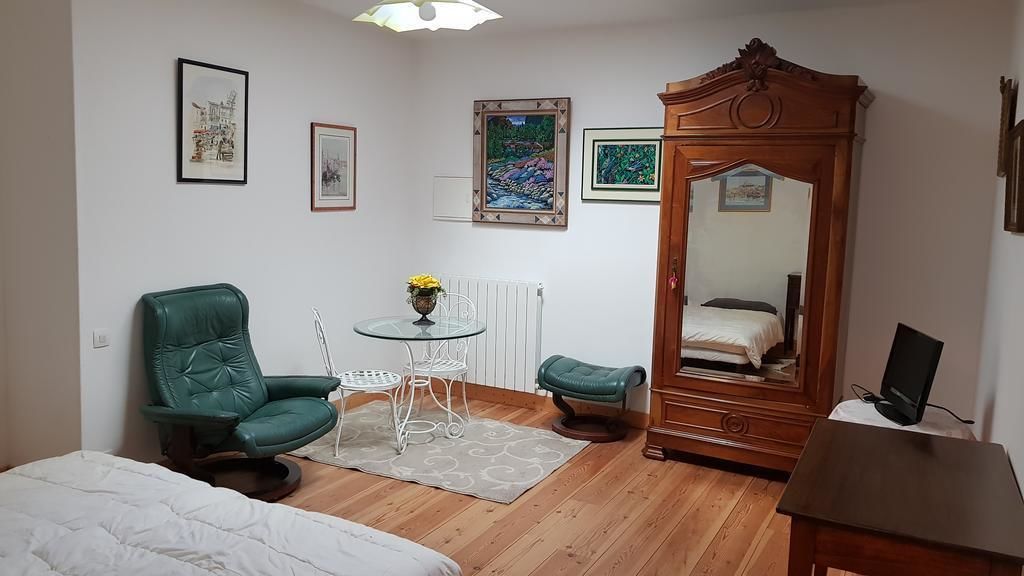 Une petite pièce bien éclairée, avec un lit, un fauteuil vert, une petite table sur laquelle se trouve un vase, un miroir et un radiateur.