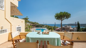 Una terraza con mesa lista para comer, con vista a una piscina y una panorámica del mar.