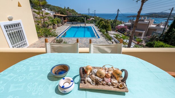 Una terraza con piscina, una mesa con una bandeja de conchas marinas y un cuenco, y vistas al mar y edificios.