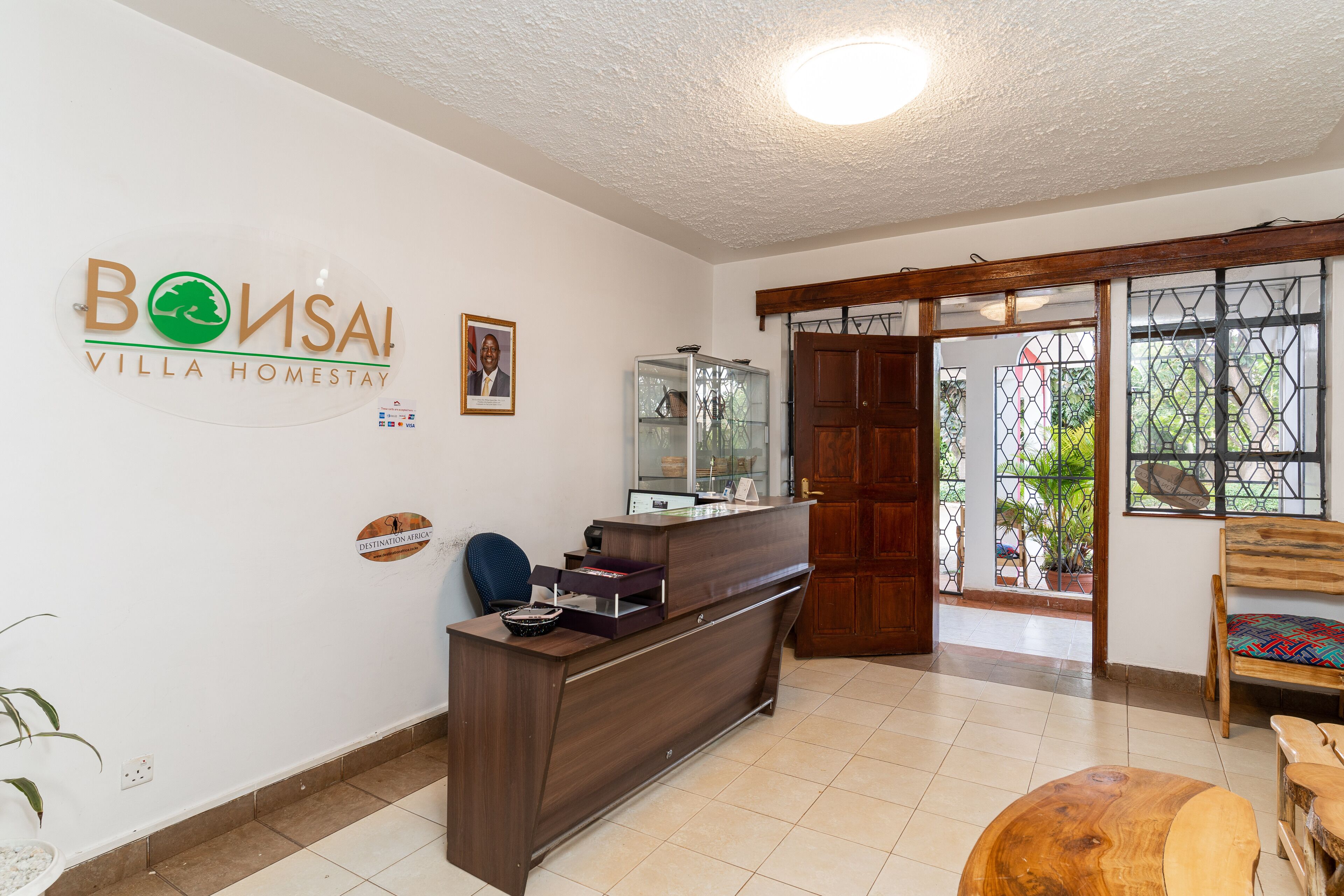 Una recepción con un cartel de Bonsai Villa Homestay, un banco de madera y un vitrina de vidrio.