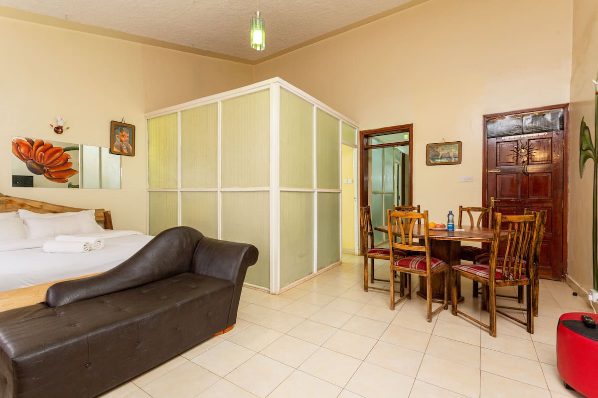 A hotel room with a bed, a sofa, a dining table with chairs, and a sliding door closet.