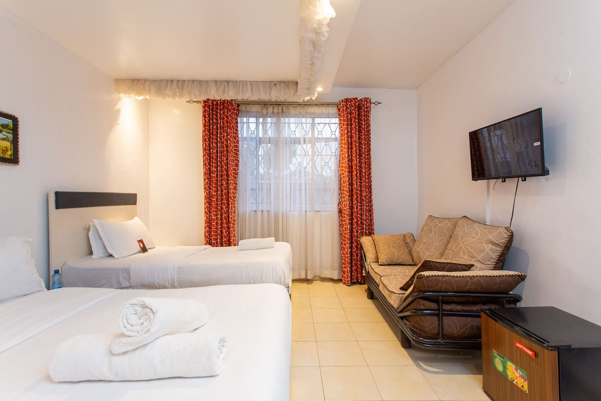 A hotel room with two beds, a sofa, a TV, and a minibar.
