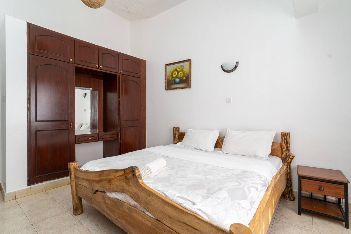 A bedroom with a wooden bed, a nightstand, a wardrobe, a mirror, and a painting on the wall.