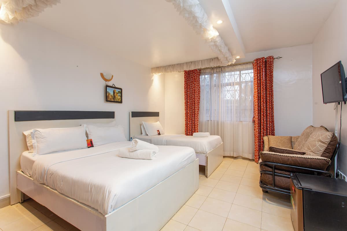 A hotel room with two beds, a sofa, a TV, and a window with curtains.
