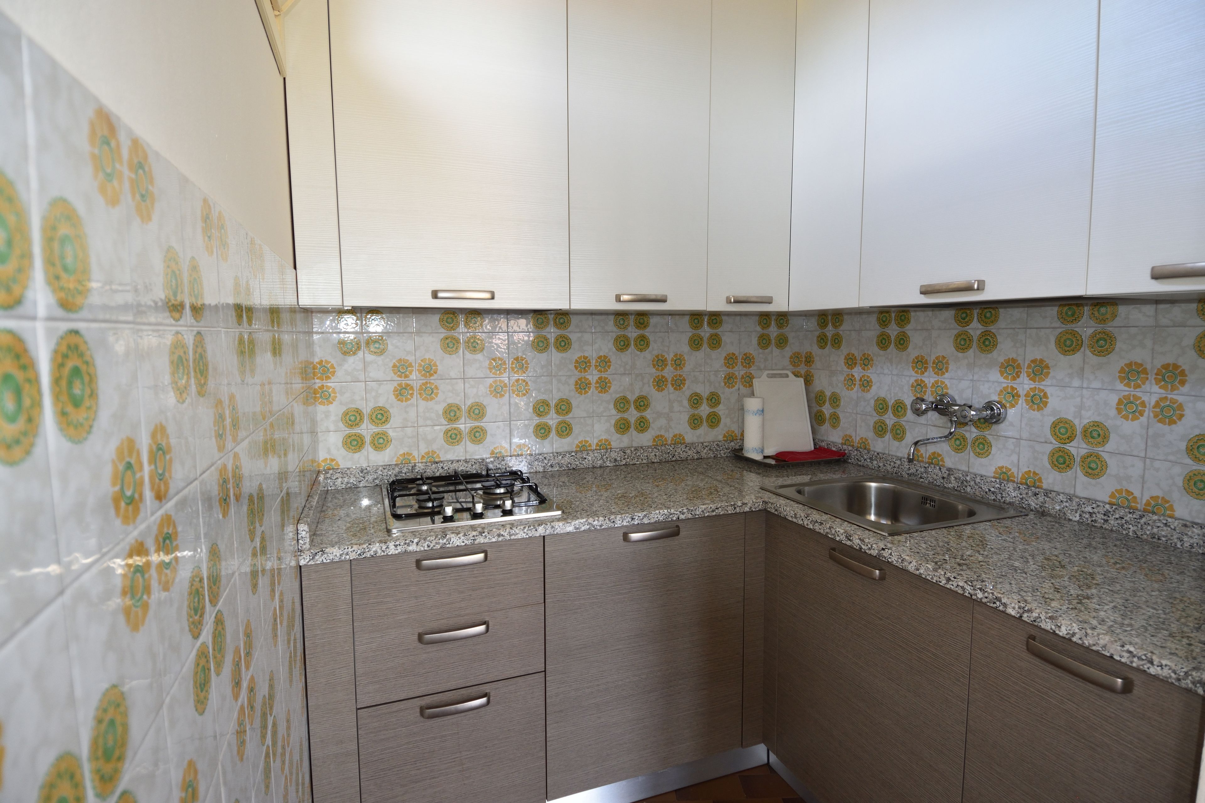 Cuina amb armaris blancs, fornel gas, rentamillera d'acer inoxidable i respatller de rajoles amb disseny.