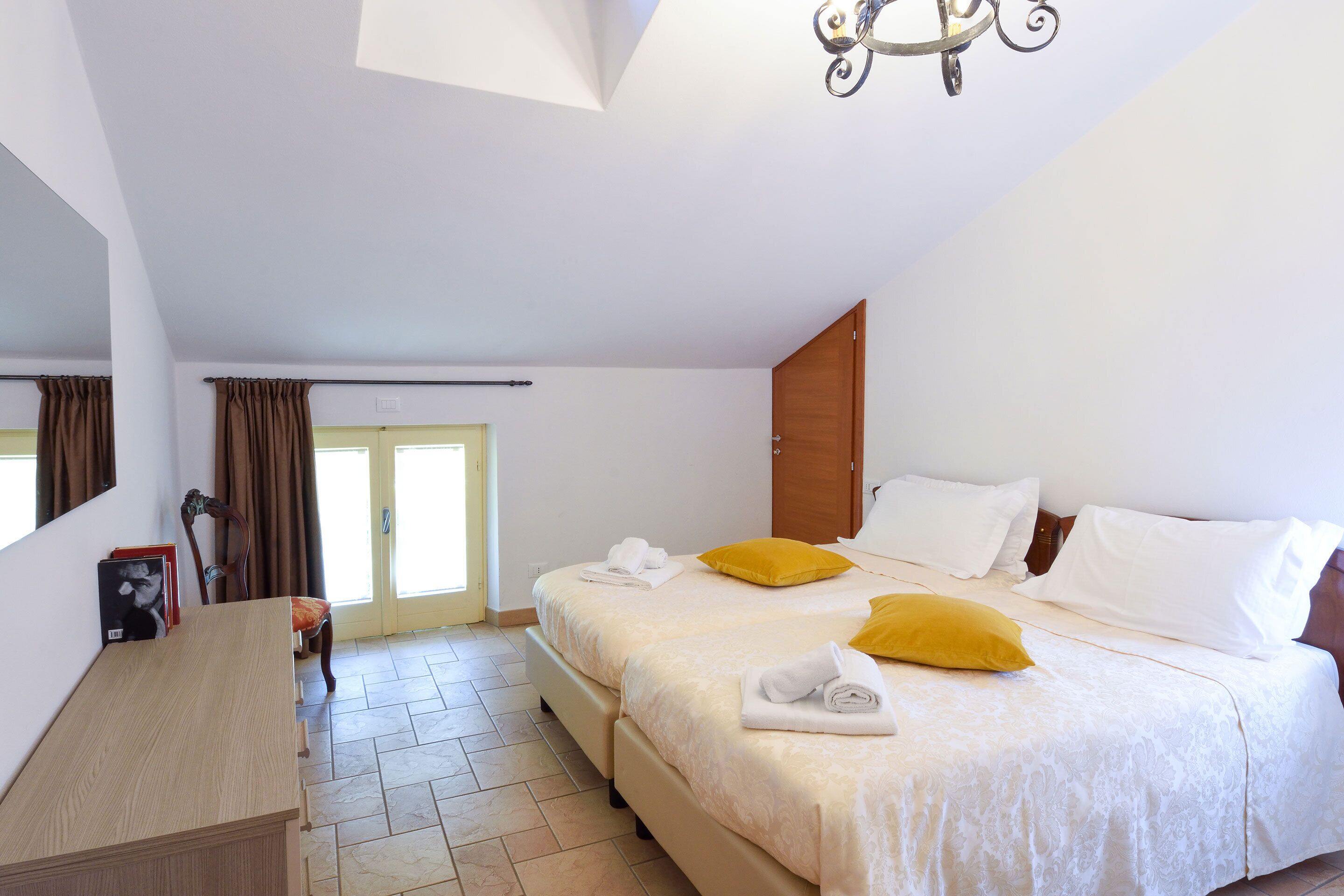 Une chambre d’hôtel avec deux lits, un bureau en bois, un miroir et une porte donnant sur l’extérieur.