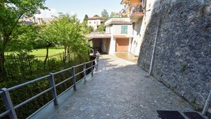 A cobblestone pathway leading to a building with a stone wall on one side and a metal railing on the other.