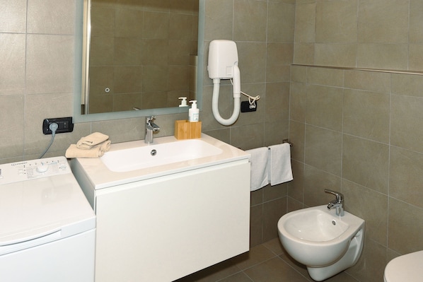 Un baño con lavamanos, espejo, toalla, bidé y lavadora.