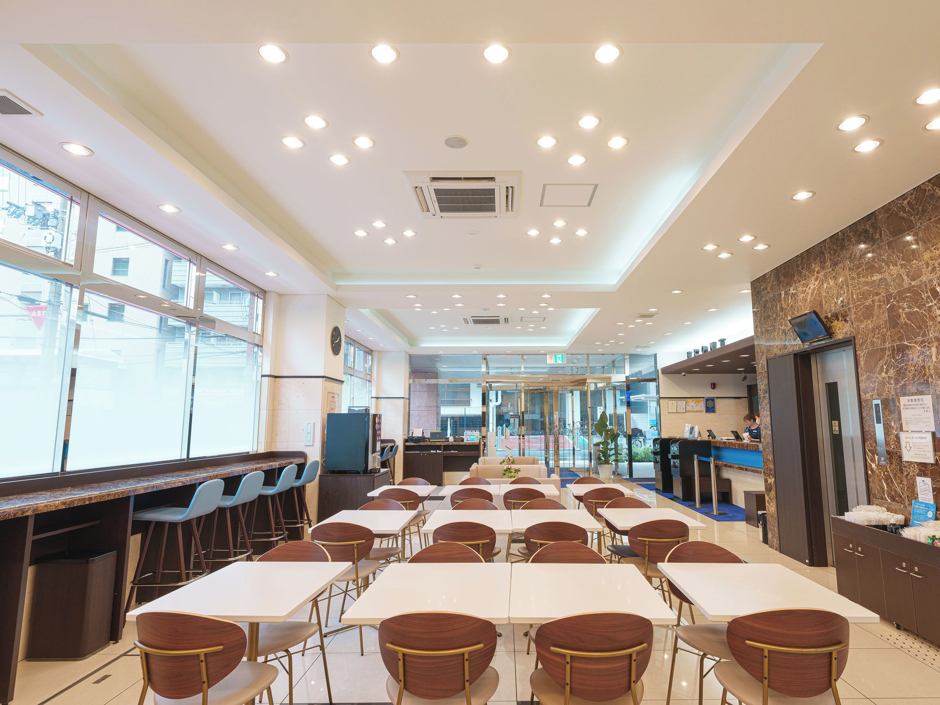 A spacious dining area with multiple tables and chairs, a reception desk, and a view through large windows.
