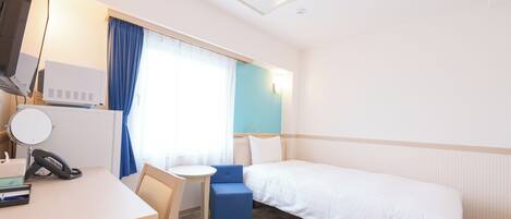 A hotel room with a bed, a desk, a chair, a small table, a telephone, and a window with curtains.