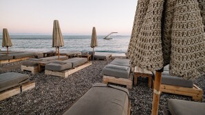 A beachside lounge area with wooden loungers and woven umbrellas, overlooking the sea. - More Meni City Beach Rhodes (Rhodes)