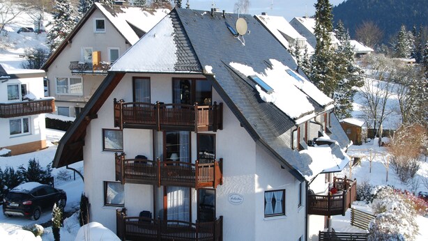 Ett hotell med flera våningar, balkonger, ett snötäckt område och en bergig bakgrund.