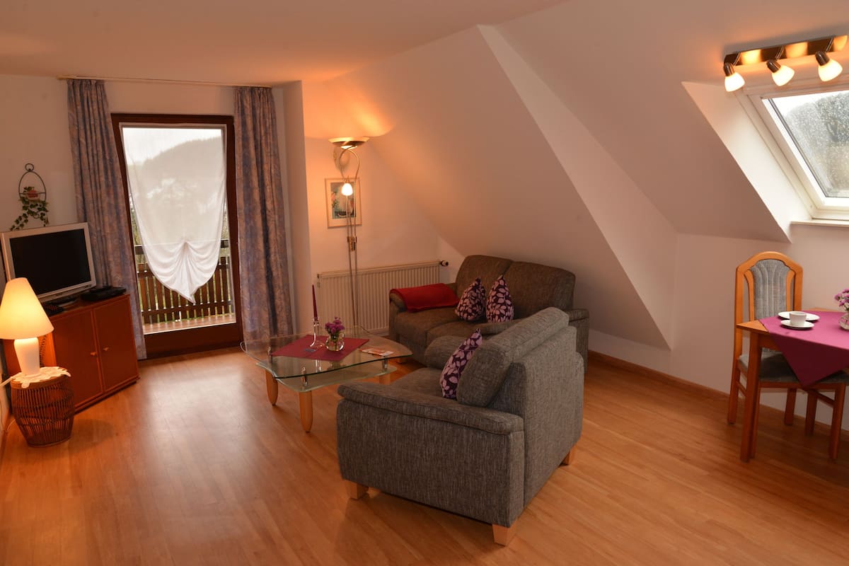 A cozy living room with a sofa, a glass coffee table, a TV, and a dining area with a table and chairs.