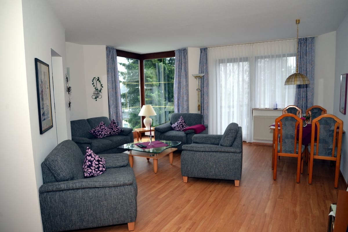A living room with two grey sofas, a glass coffee table, and a dining area with wooden chairs and a table.