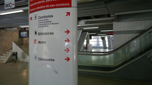 A directional sign in a subway station with arrows pointing to various facilities such as restrooms, elevators, and metro services.