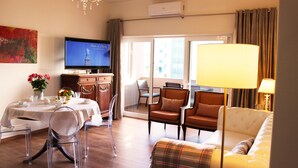 A hotel room with a television, a dining table with chairs, a sofa, and a lamp. - QUAD 3 Apartment with Balcony, Air Conditioned, Garage, City view, 24/7 security (Lisbon)