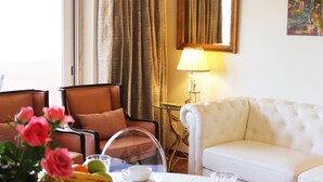 A hotel room with a white sofa, a brown armchair, a glass table with a tea set, and a vase of pink flowers. - QUAD 3 Apartment with Balcony, Air Conditioned, Garage, City view, 24/7 security (Lisbon)
