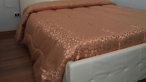 A bedroom with a white headboard, a brown patterned bedspread, and two wall-mounted lights.