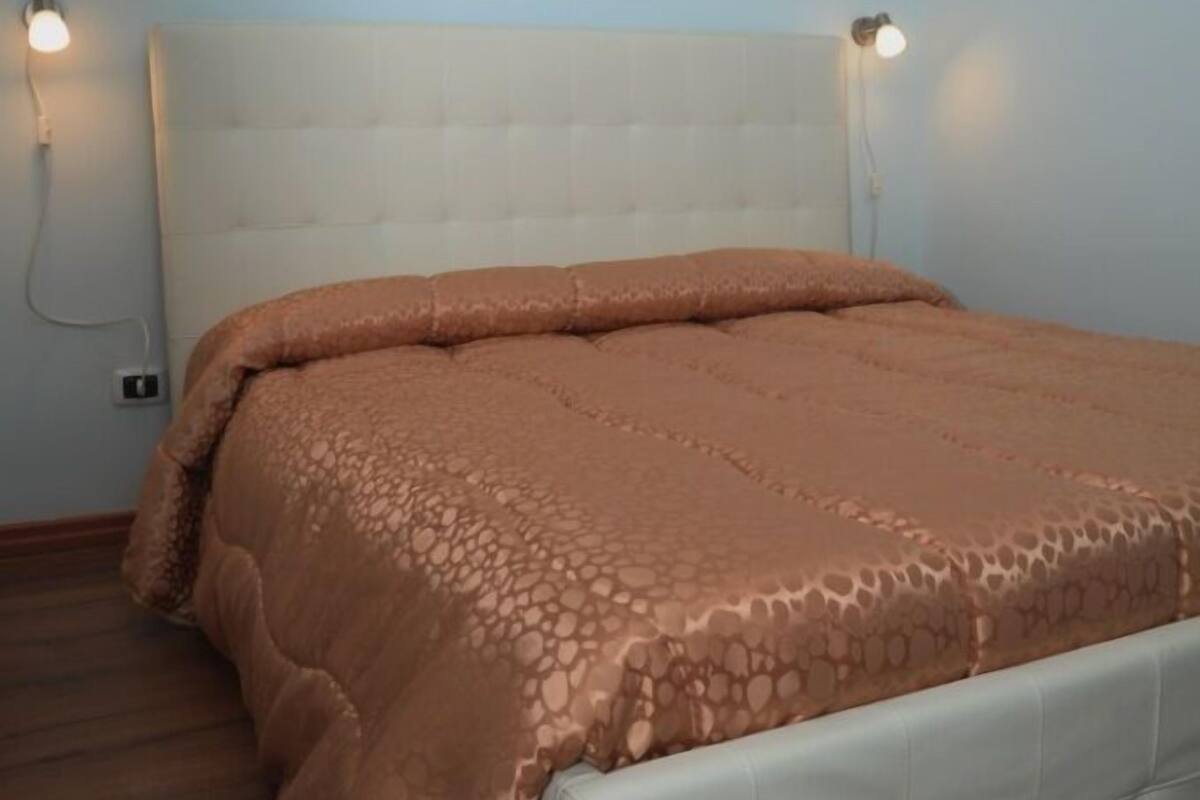 Ein Schlafzimmer mit weißem Kopfteil, einer braunen Bettdecke mit Muster und zwei Wandlampen.