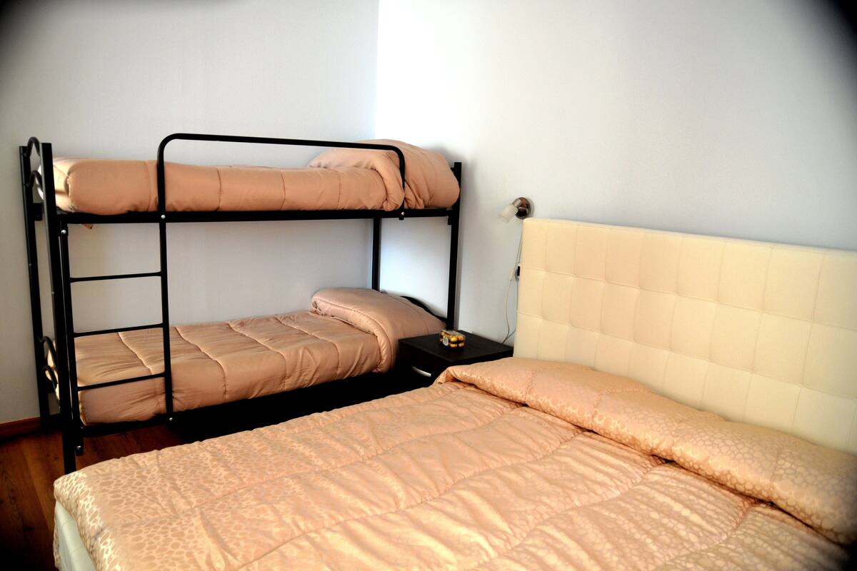 Ein Stockbett mit einem unterem Bett und einem Einzelbett, beide mit passender beige Bettwäsche.