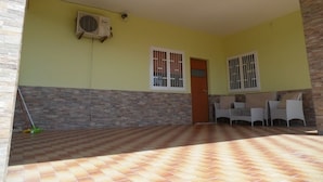 A covered patio area with a tiled floor, a stone wall, and a door leading inside.