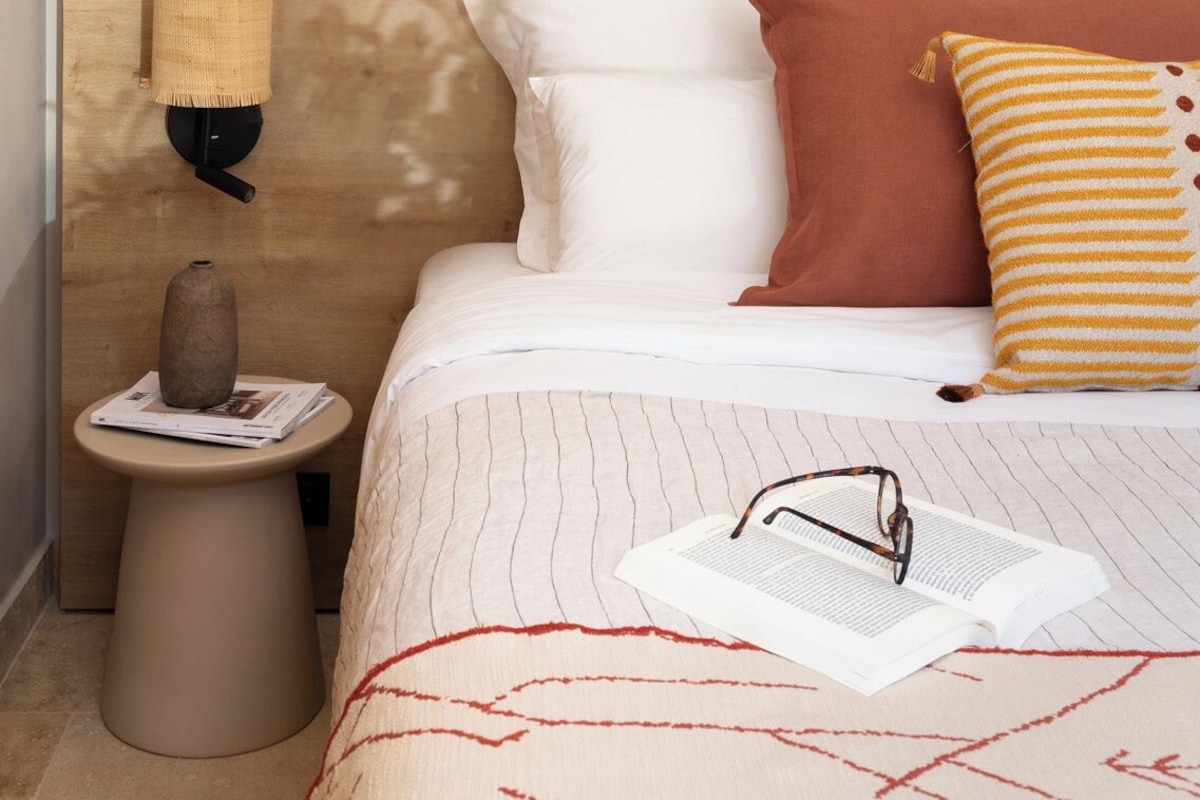Ein Schlafzimmer mit Bett, Kissen, einem Nachttisch mit Vase sowie einem an der Wand befestigten Haken für Hüte.