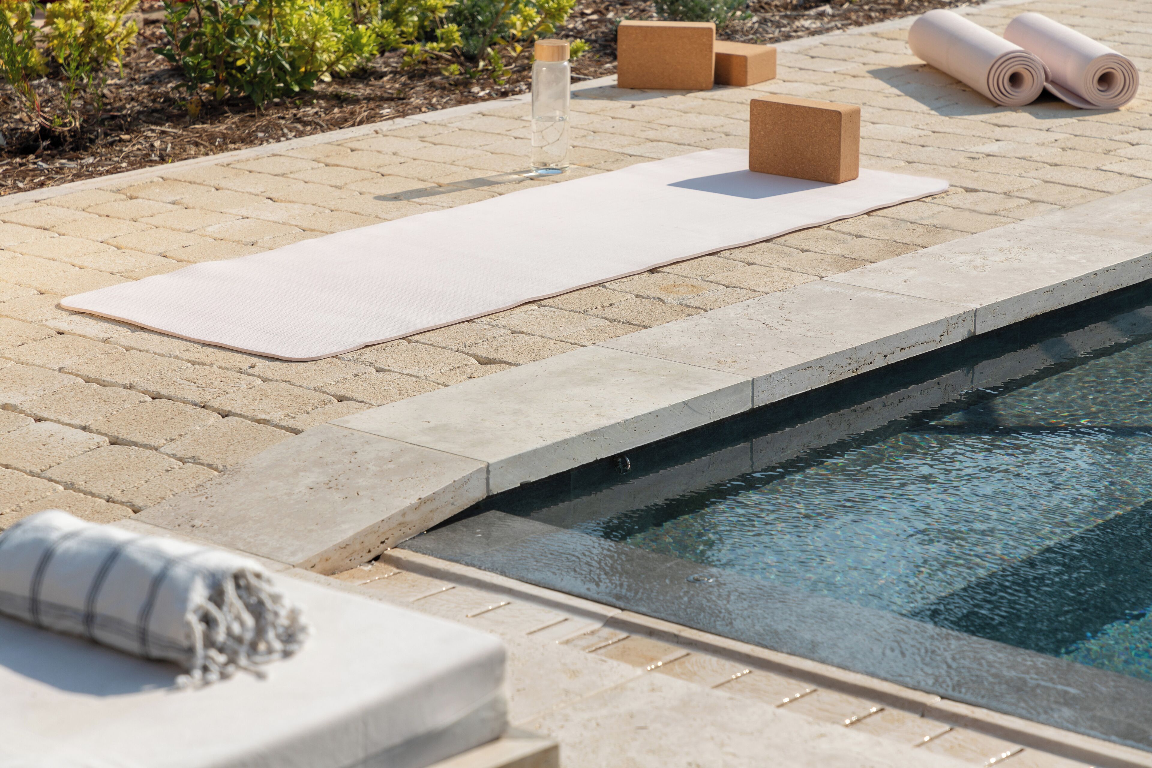 A poolside area with a yoga mat, a rolled-up towel, and a water bottle.