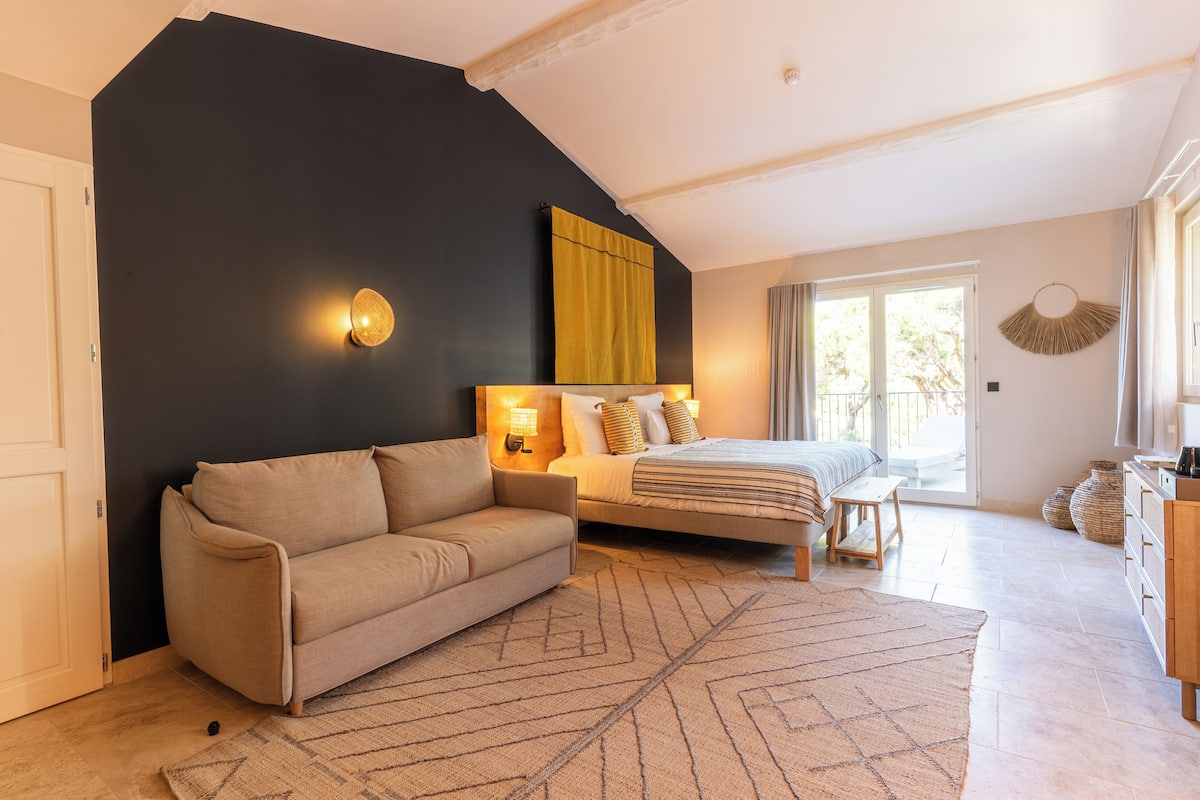 A bedroom with a bed, a sofa, a nightstand, and a large window.