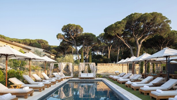 A poolside area with lounge chairs and umbrellas, surrounded by trees and a stone wall. - Hôtel L'Escalet  (Ramatuelle)