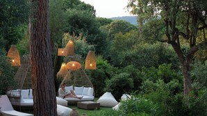An outdoor seating area with wicker furniture, hanging lights, and a large tree trunk. - Hôtel L'Escalet  (Ramatuelle)
