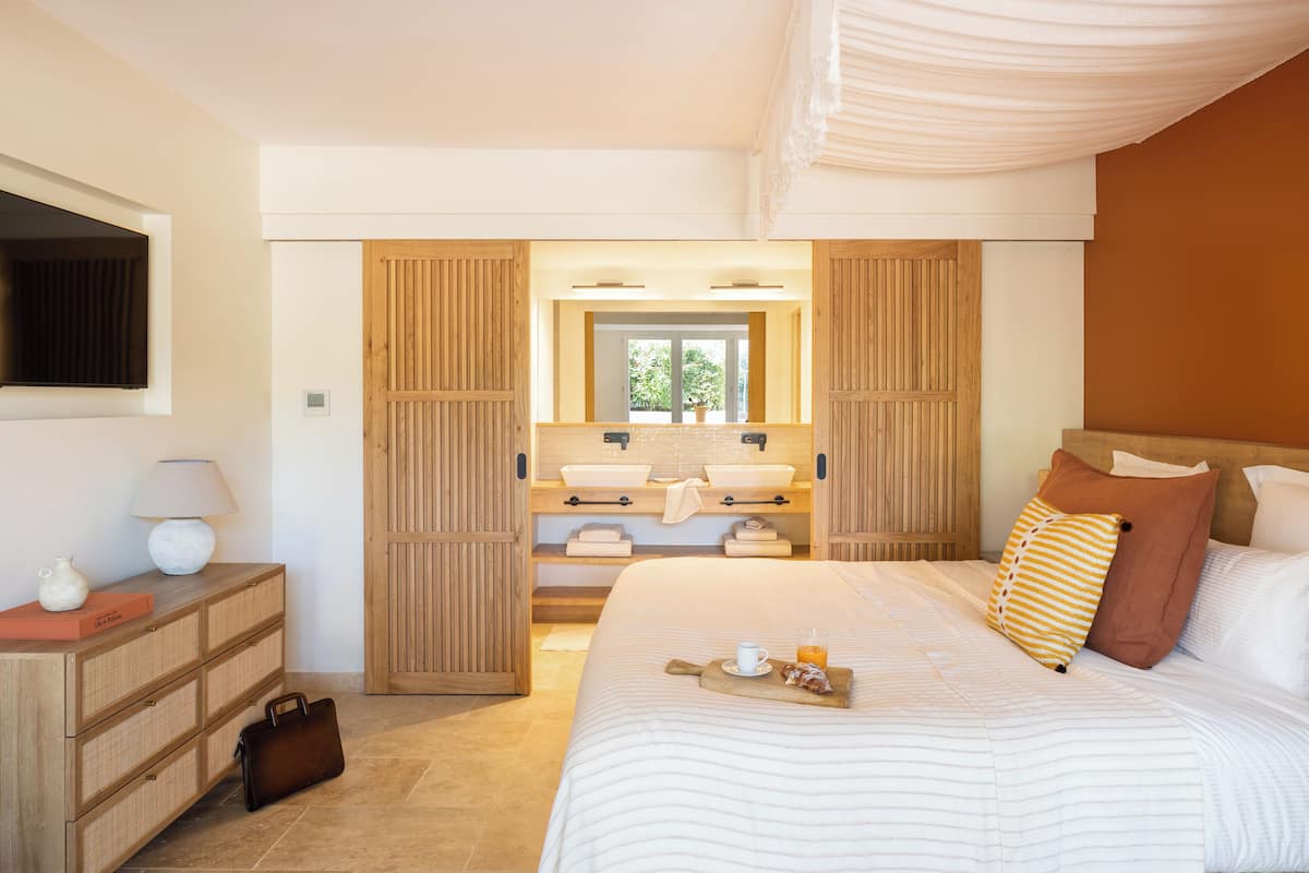 A bedroom with a large bed, a bedside table with a lamp, a dresser, and a mirror.