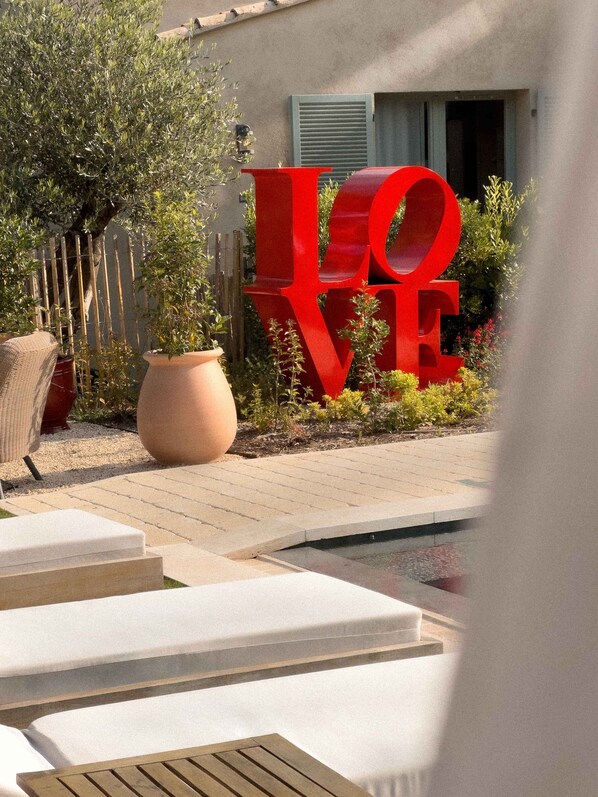 A pool area with a large red 'LOVE' sign, outdoor seating, and a potted plant.