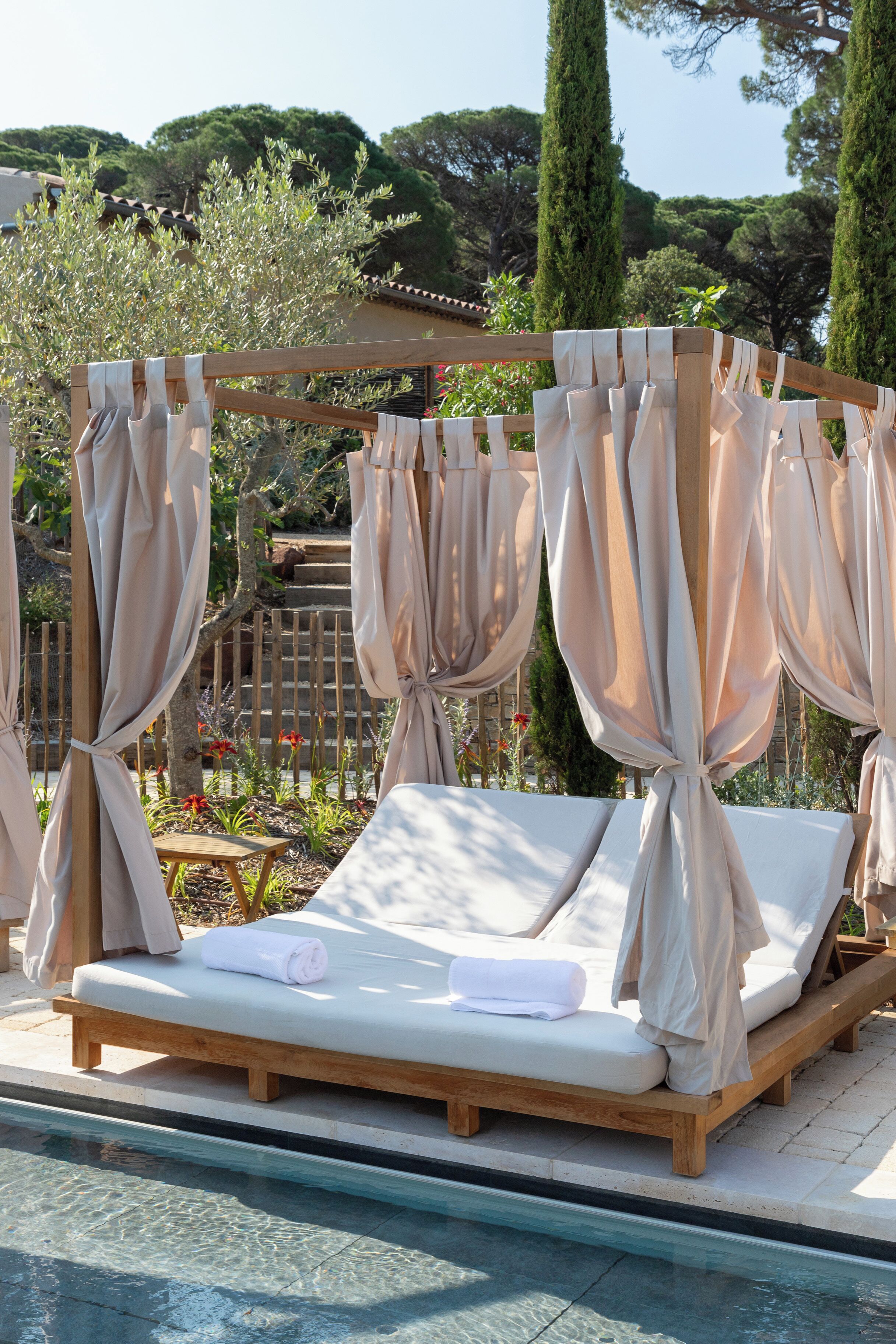 A poolside lounge area with wooden loungers and beige curtains.