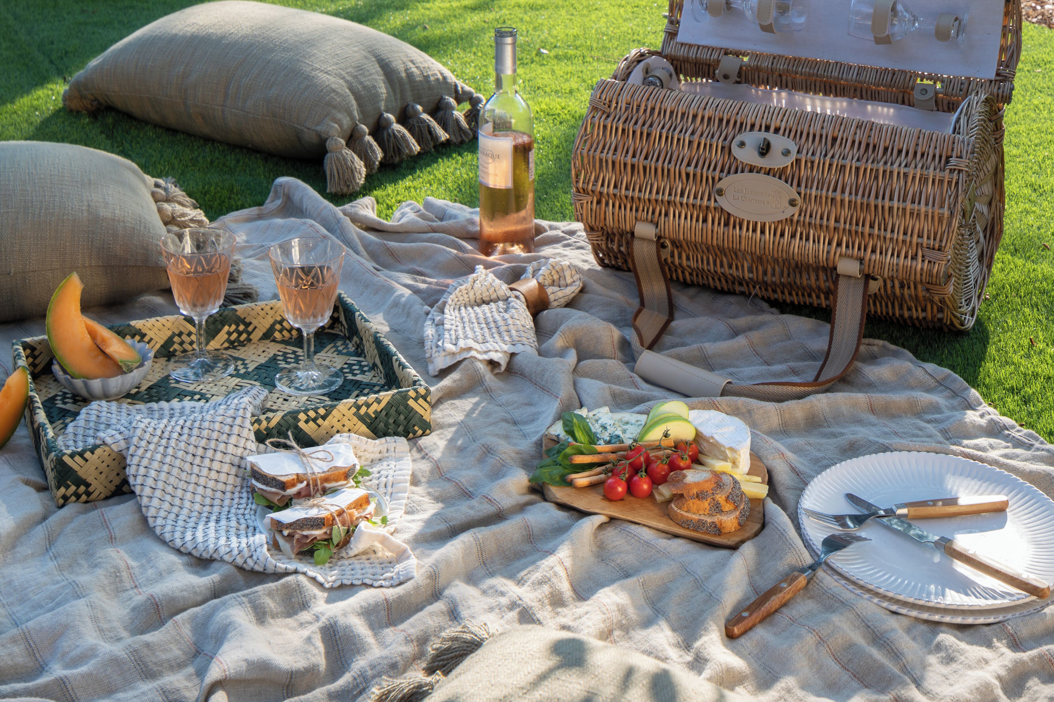 Ein Picknick auf einer Wiese mit Korb, Decke, Speisen und einer Flasche.