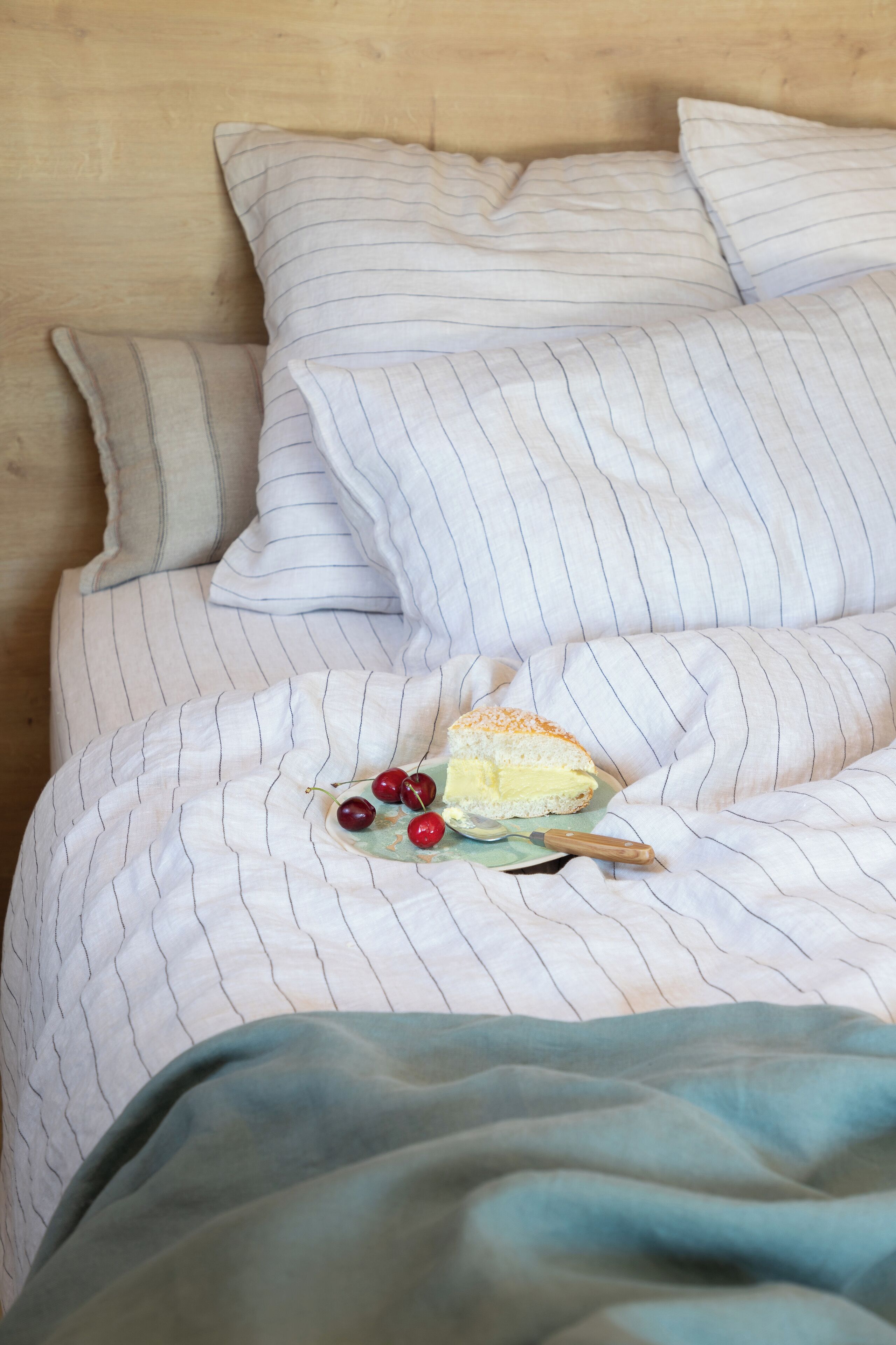 Una cama con ropa de cama a rayas, una almohada y un plato con un pastel y cerezas.