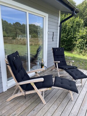 Une terrasse avec deux chaises longues et une table sur laquelle se trouvent une bouteille et des verres.