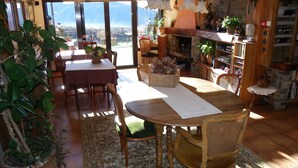 Un comedor acogedor con una mesa y sillas de madera, rodeado de plantas en macetas y vistas a montañas a través de amplios ventanales.