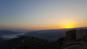 A sunset view from a building overlooking a valley with a body of water and distant mountains. - Casa Churchill (Conca de Dalt)